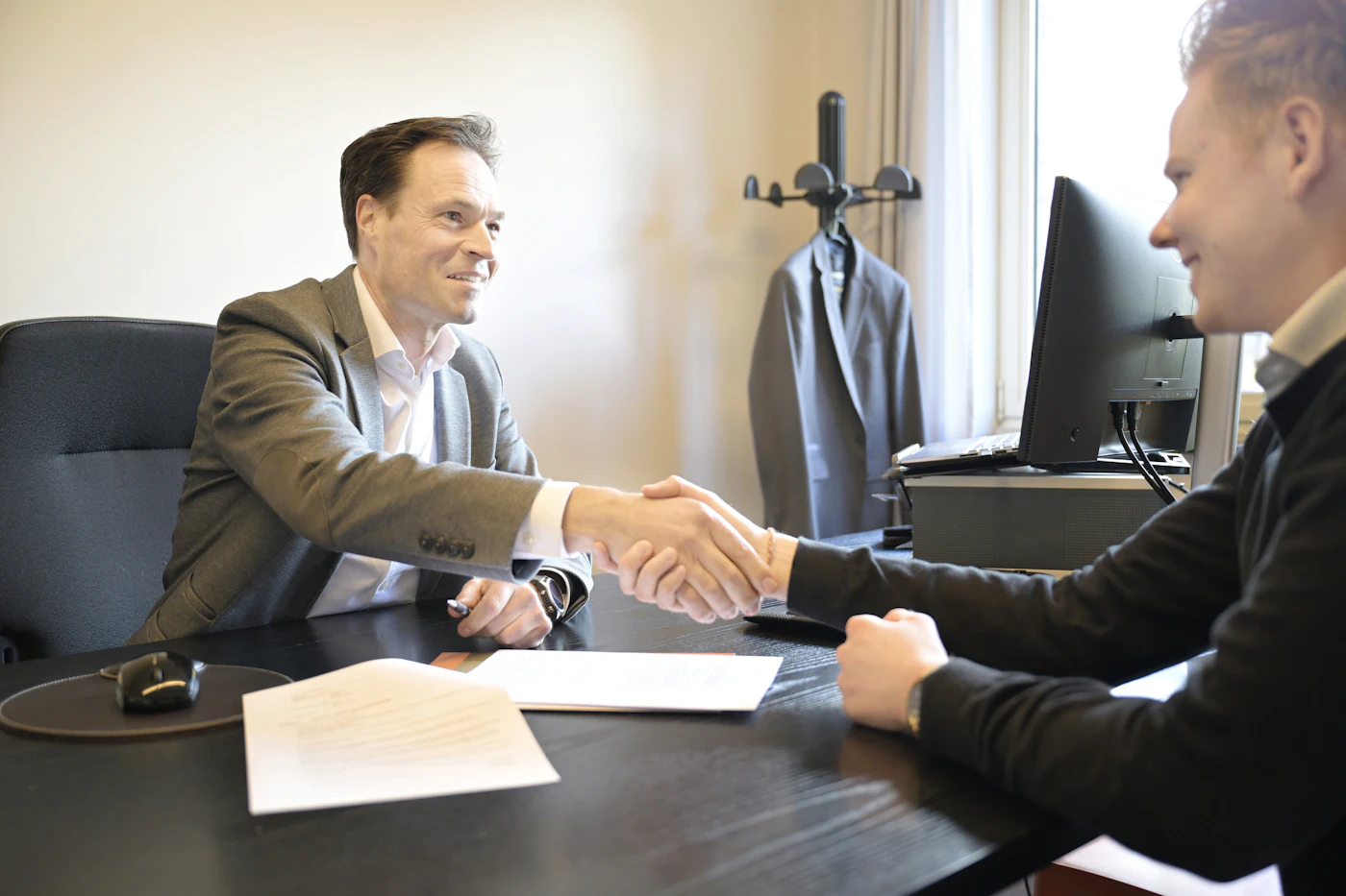 Two people shaking hands across a desk in an agency office