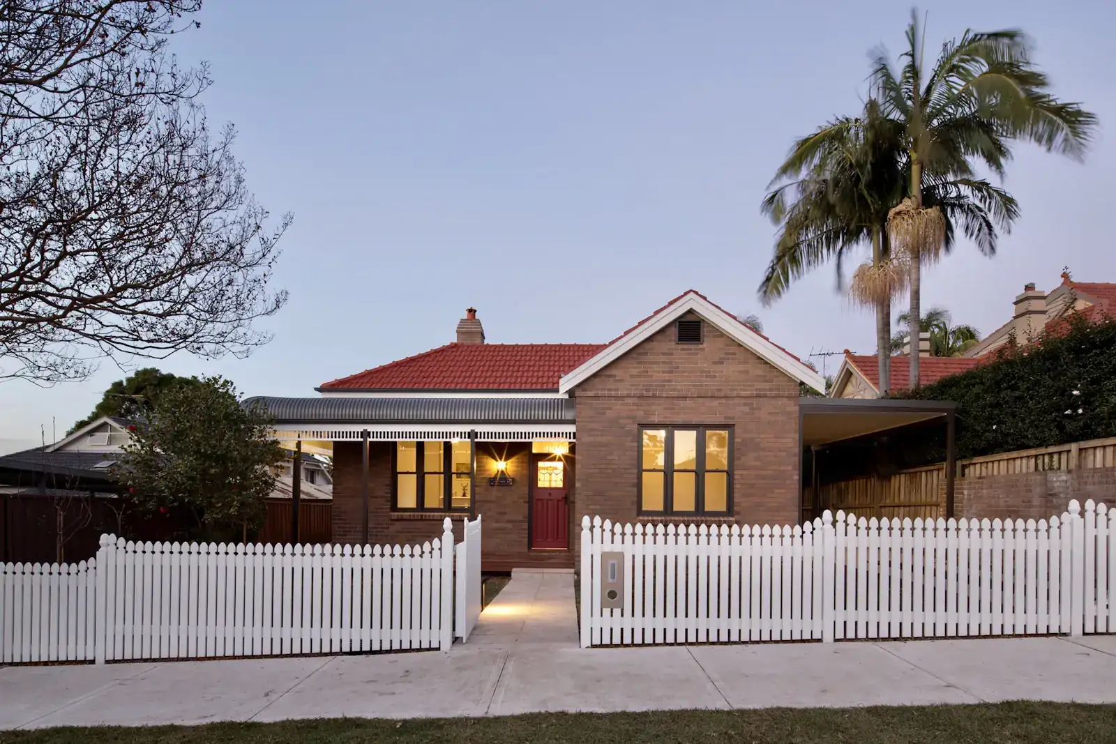 A Queenslander home with a white picket fence, lit at dusk